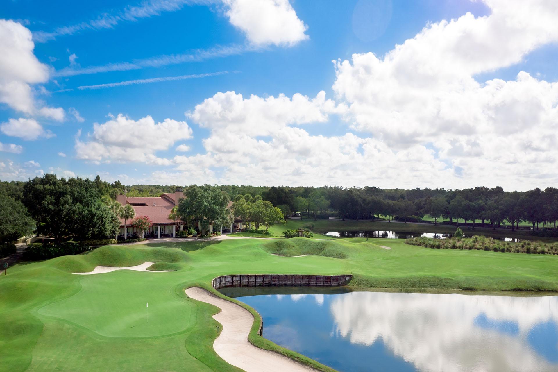 A pristine green sits beside a calm pond with the clubhouse visible in the background.