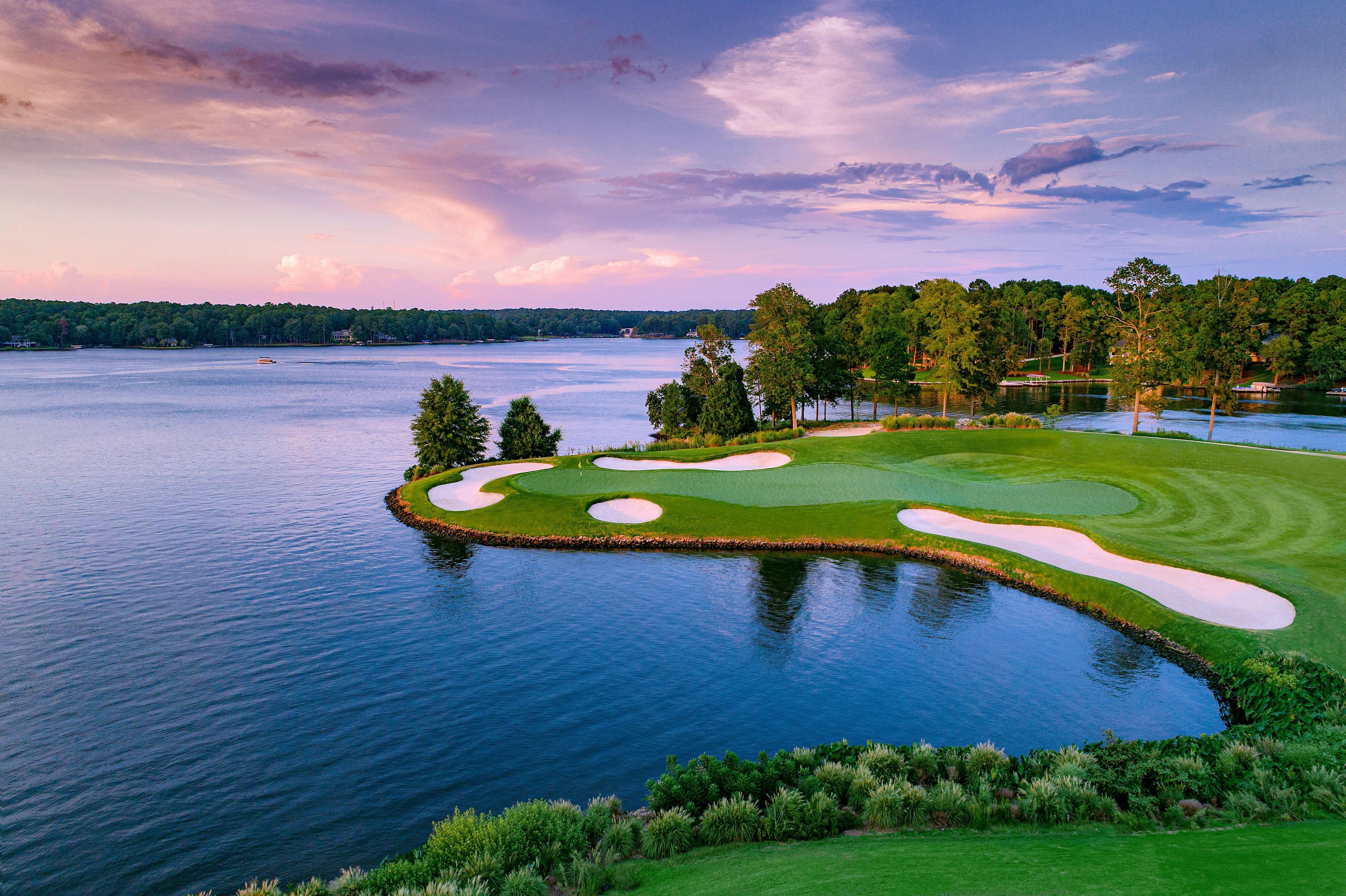A stunning lakeside green surrounded by sand traps under a colorful sunset sky.
