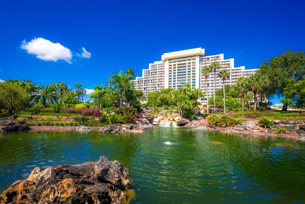 Exterior view of the Hyatt Regency Grand Cypress hotel building with its logo in bold writing at the top and a lovely garden which leads to a pond