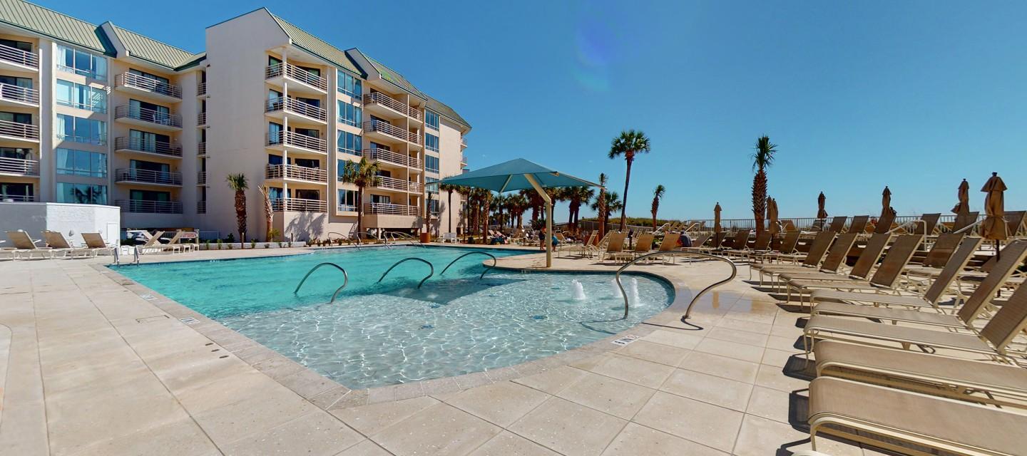 Sun beds surrounding swimming pool at the resort while the hotel building towers over