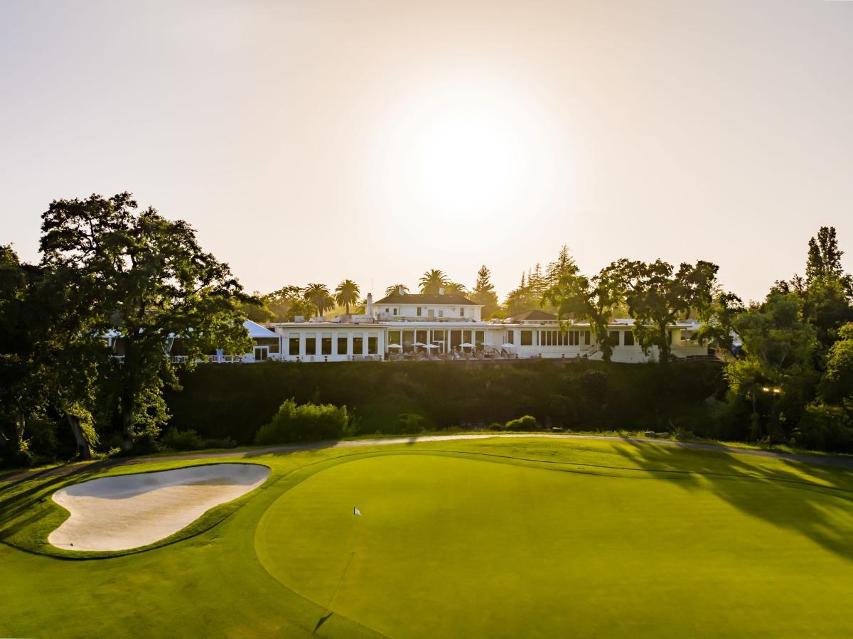 Sun shining over the resort building onto a smooth green with a sand bunker
