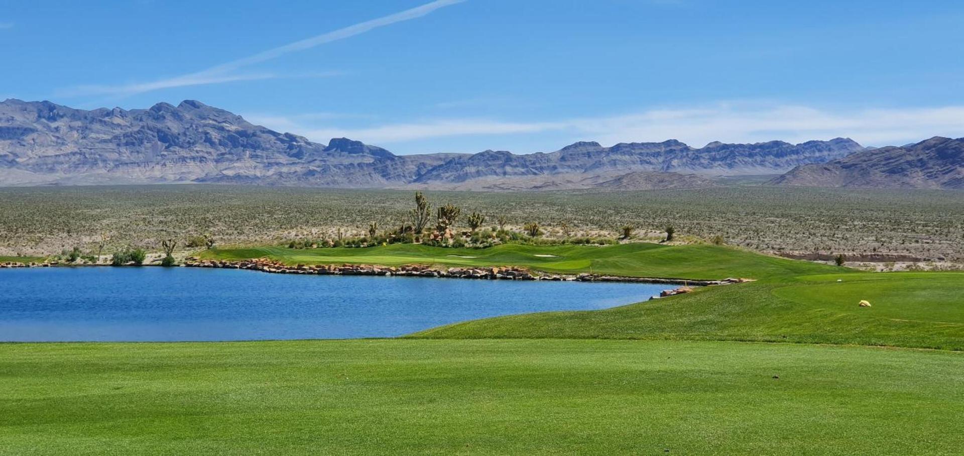 A pristine lake alongside a golf course with distant desert mountains.