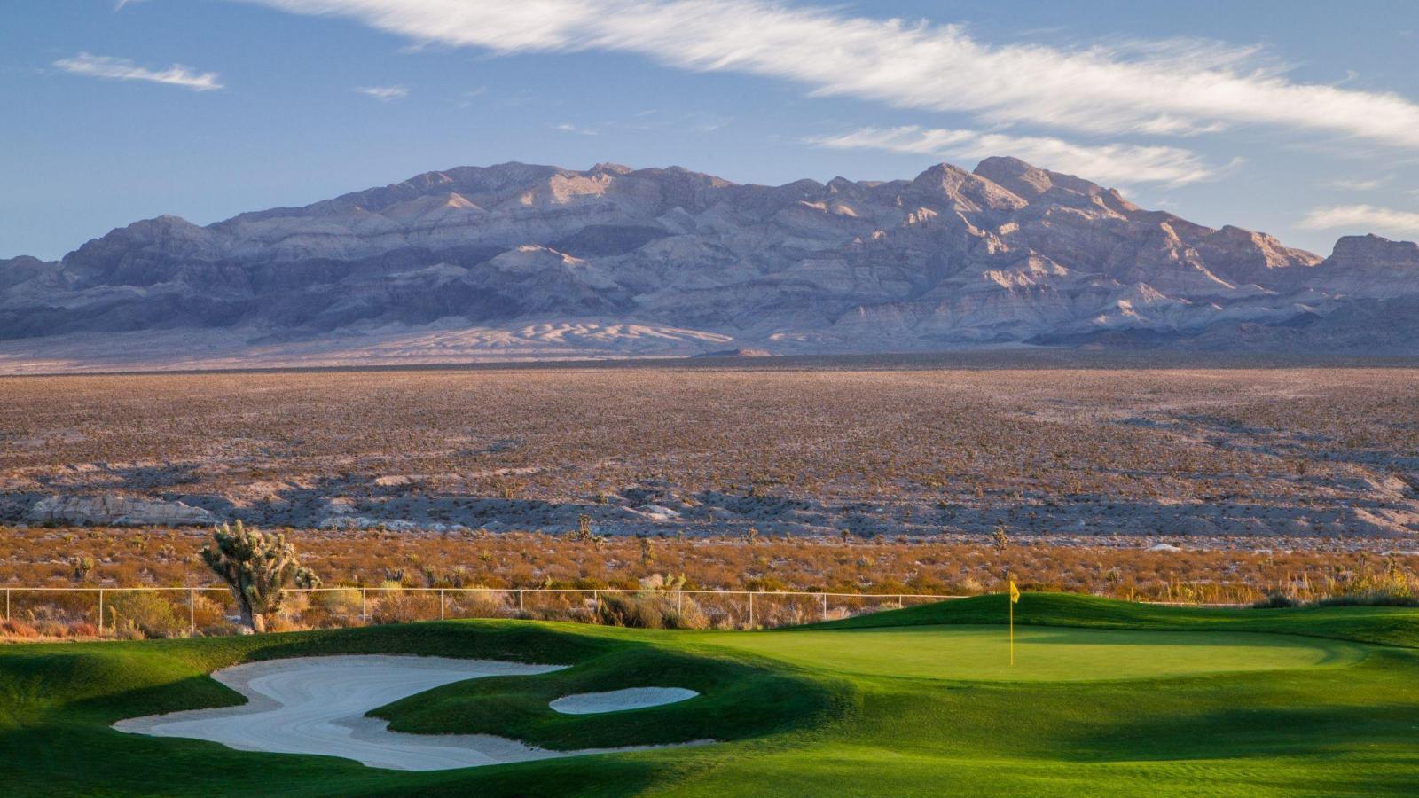 An extreme mountain overlooking a smooth green with a sand bunker placed next to it