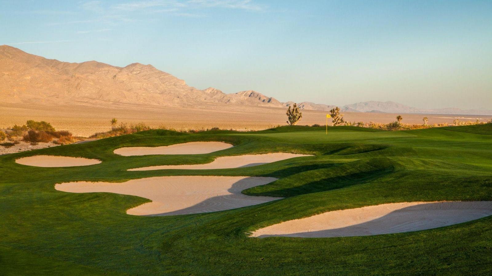 Five uniquely shaped sand bunkers placed next to a smooth green under blue skies