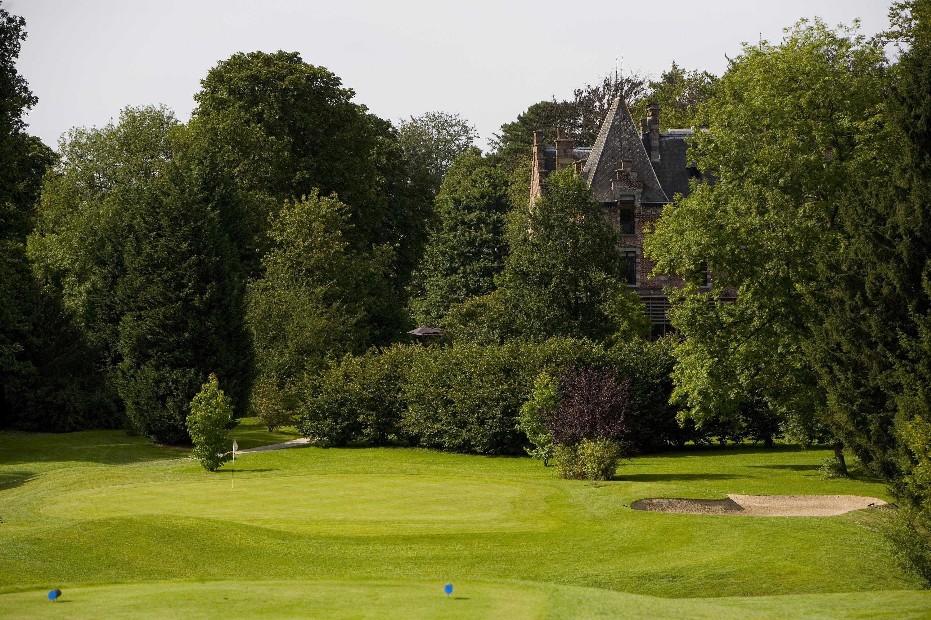 The Golf Club 7 Fontaines clubhouse peaking through the trees surrounding a well-maintained green