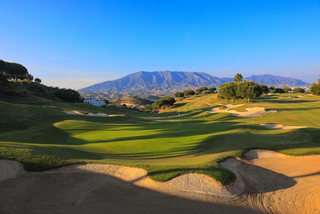 Green surrounded by bunkers in the foreground, mountains and blue sky in the background
