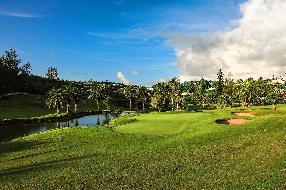 A serene golf hole framed by palm trees and a reflective pond.