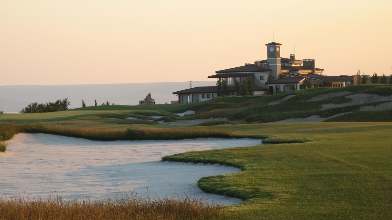 A large sand bunker placed on a well-maintained fairway leading towards the resort building