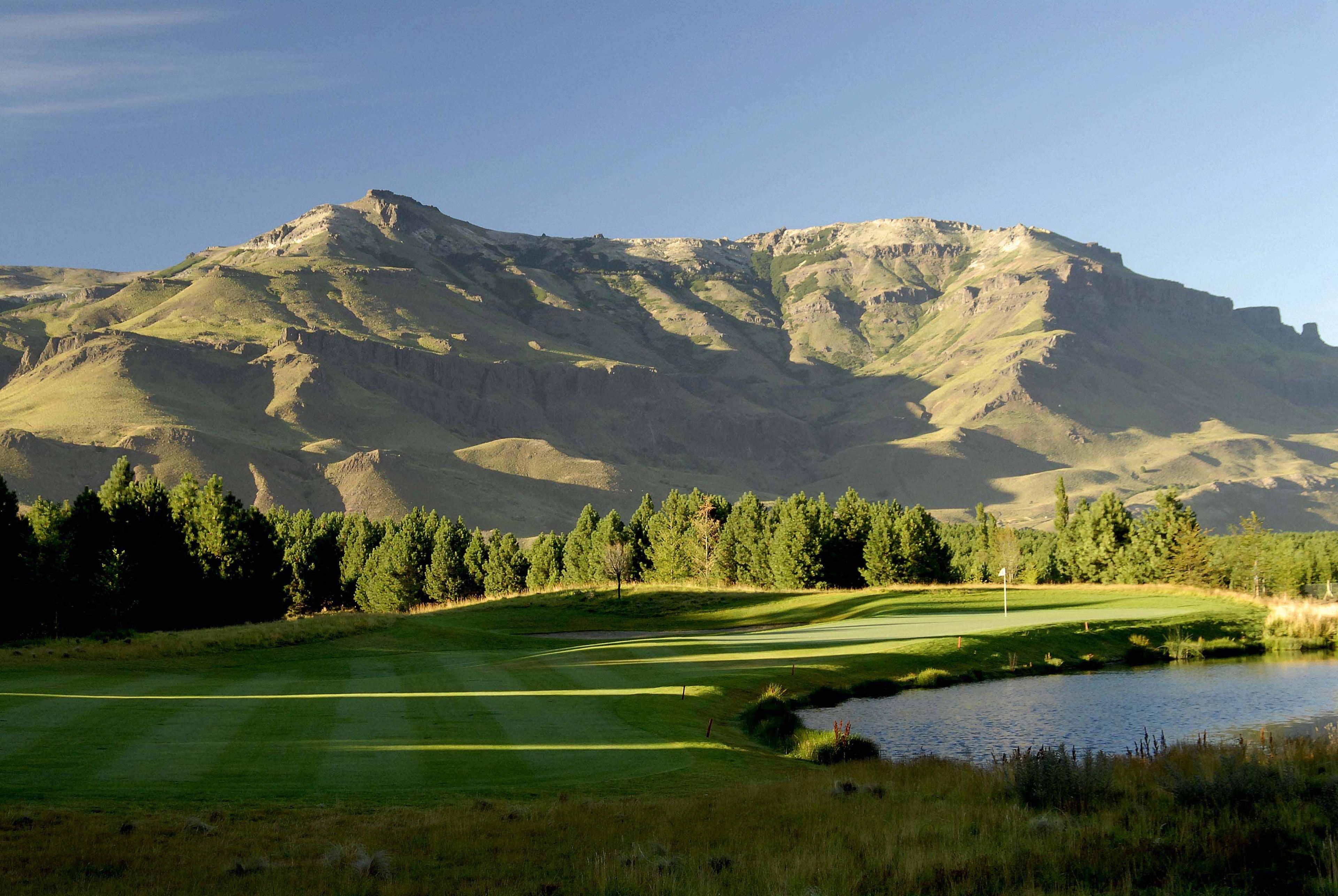 A winding fairway leading to a smooth green with mountain views