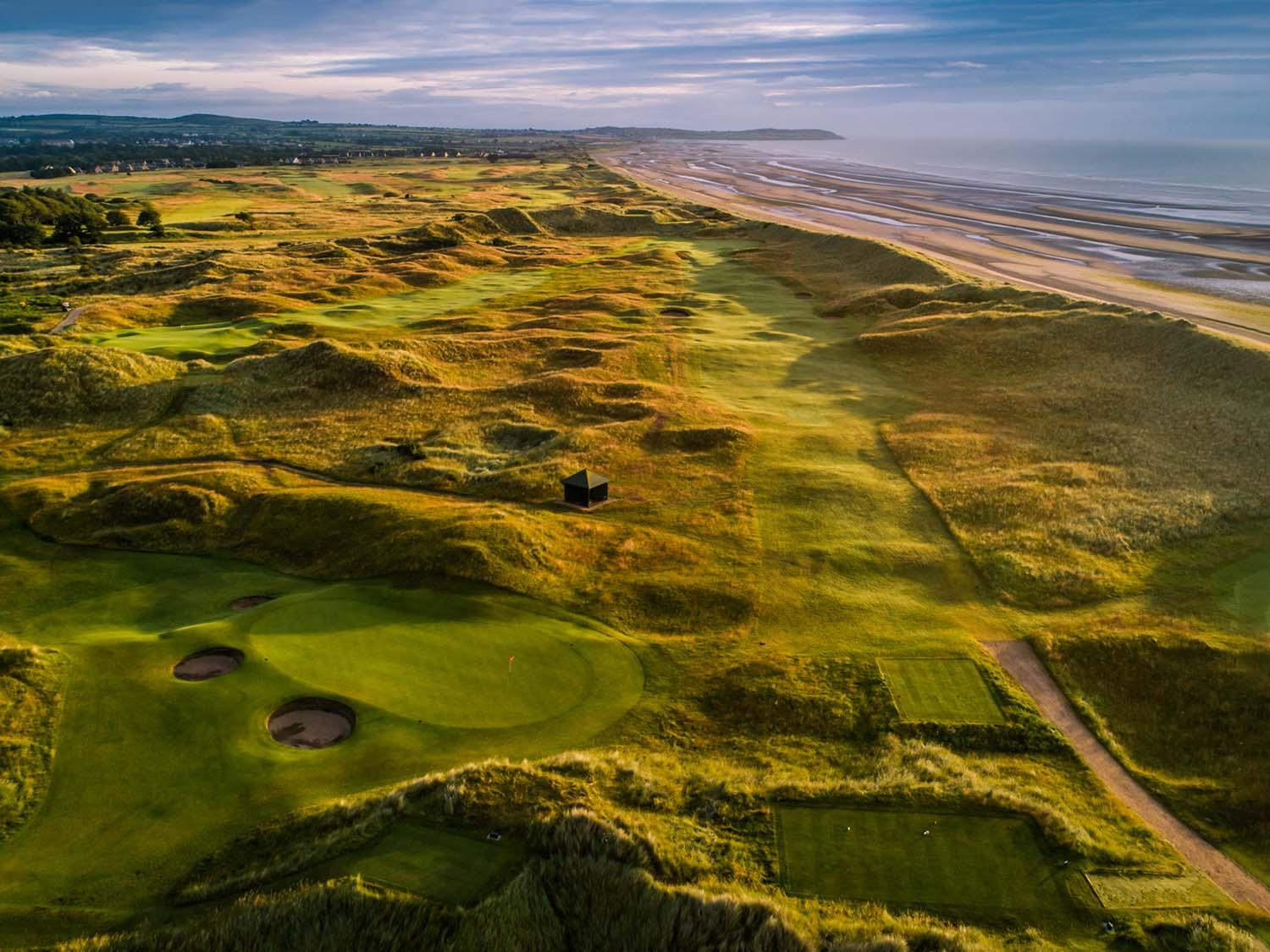 A sweeping coastal golf course surrounded by golden dunes and a wide beach.