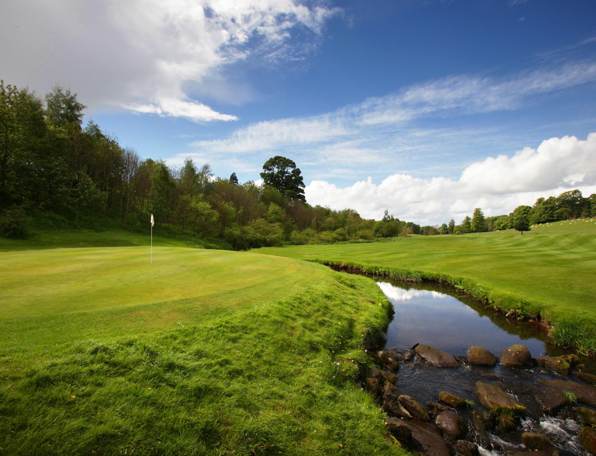 A serene green beside a winding stream under a bright blue sky.