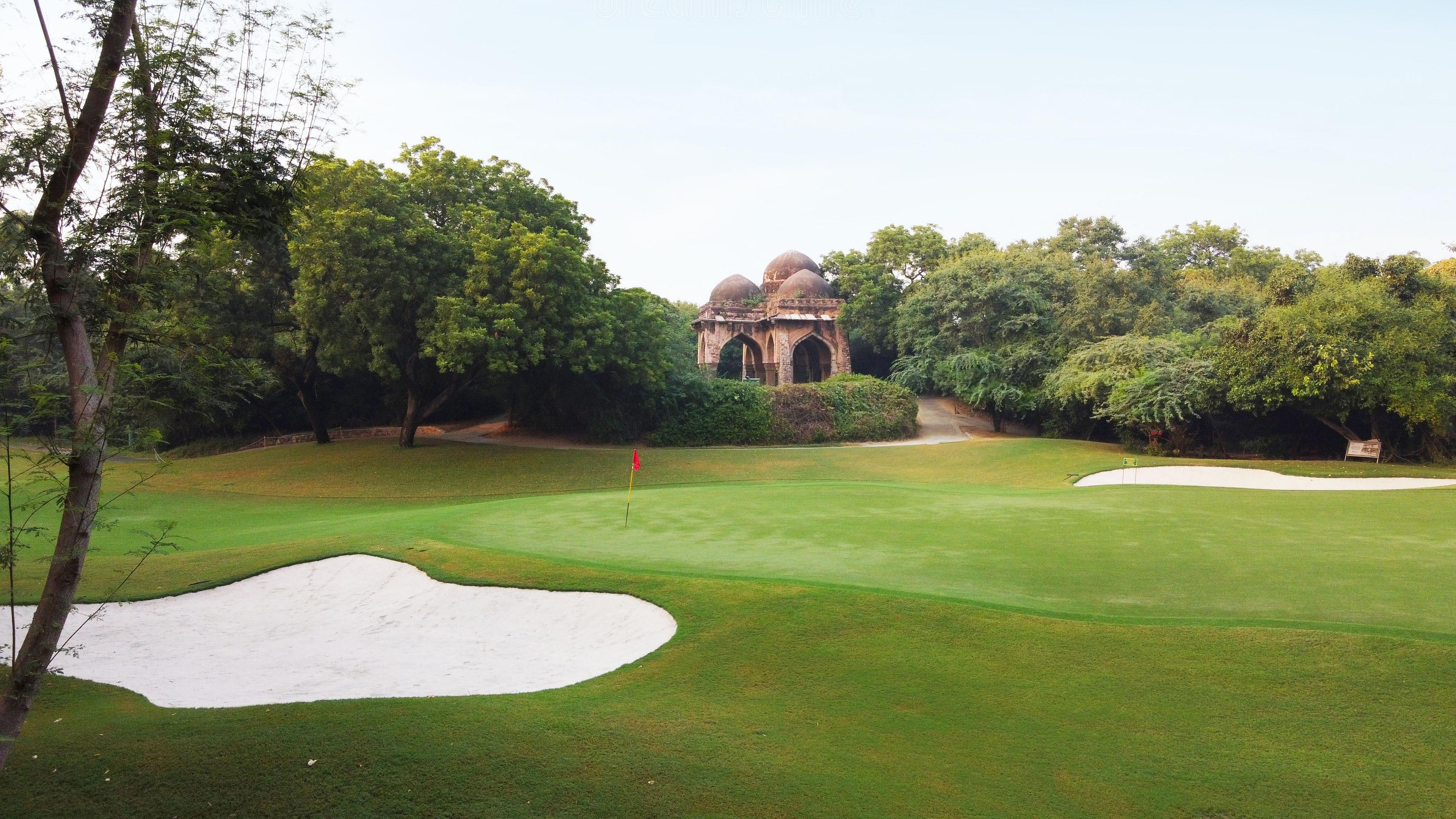 A green lies near a historic stone building with sand bunkers nearby.