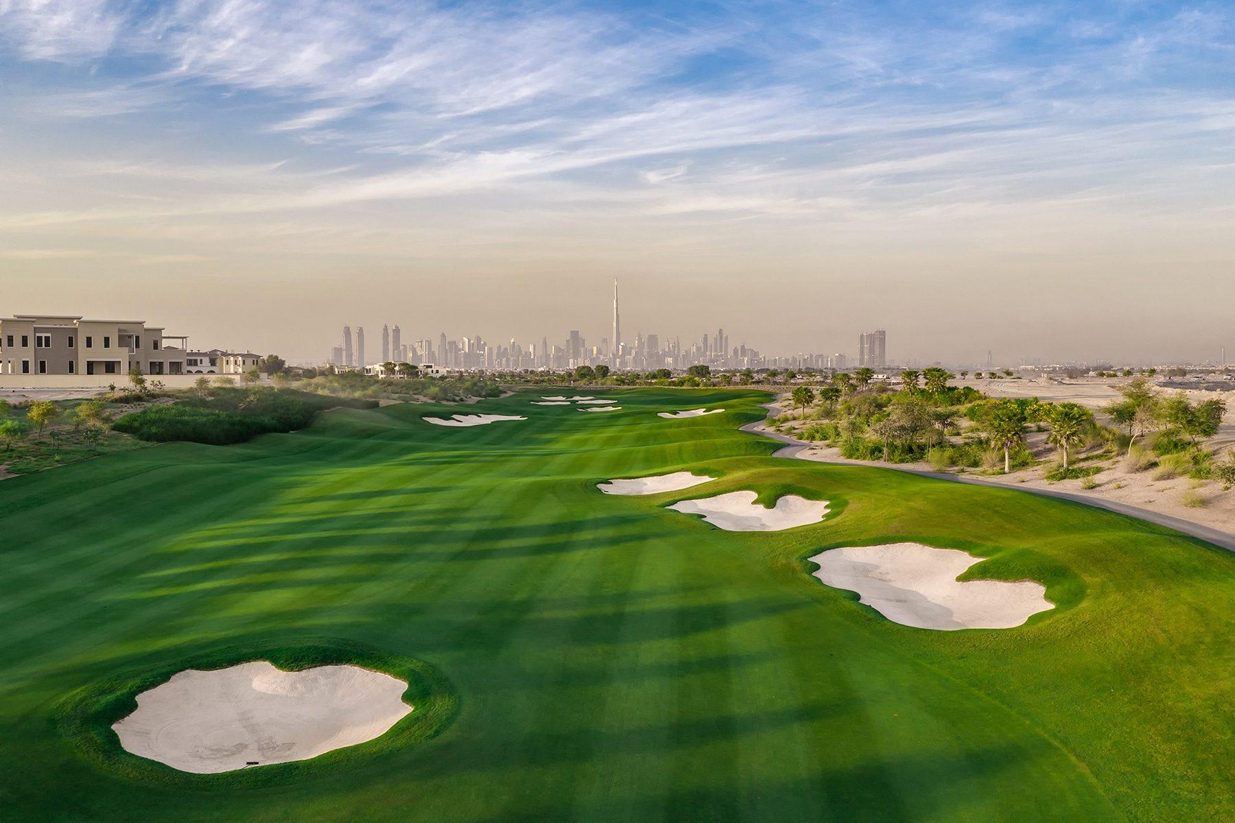 A wide fairway littered with sand bunkers and distant city views