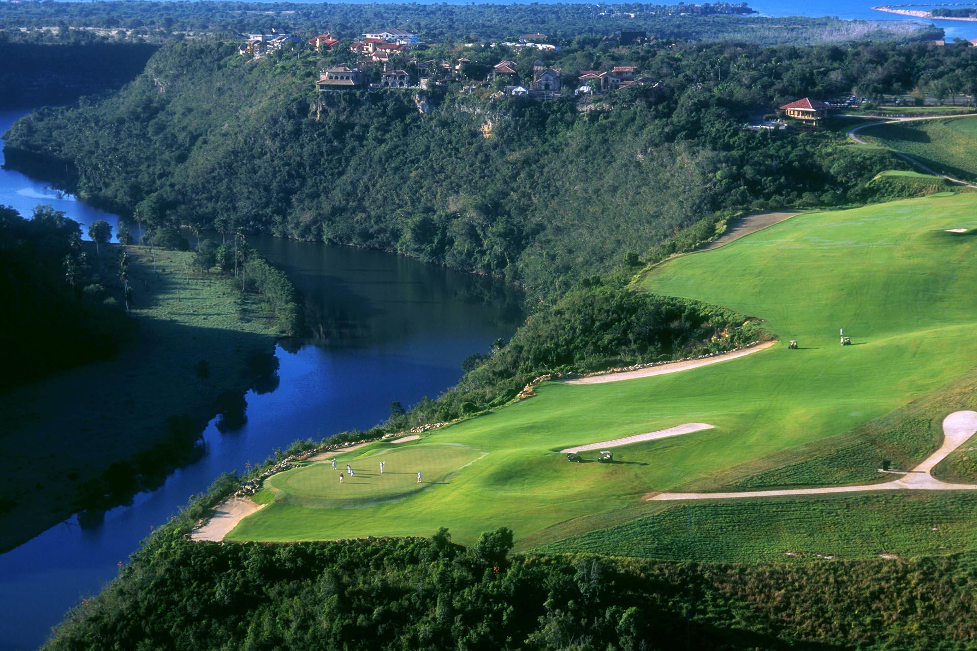 A well maintained green placed at the end of a downhill fairway with golfers enjoying their round
