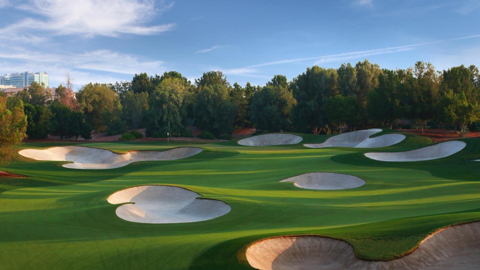 A smooth green littered with large sand bunkers framed by forest trees