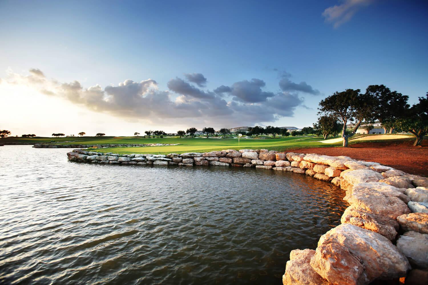 A rocky shoreline borders the calm water near the green.