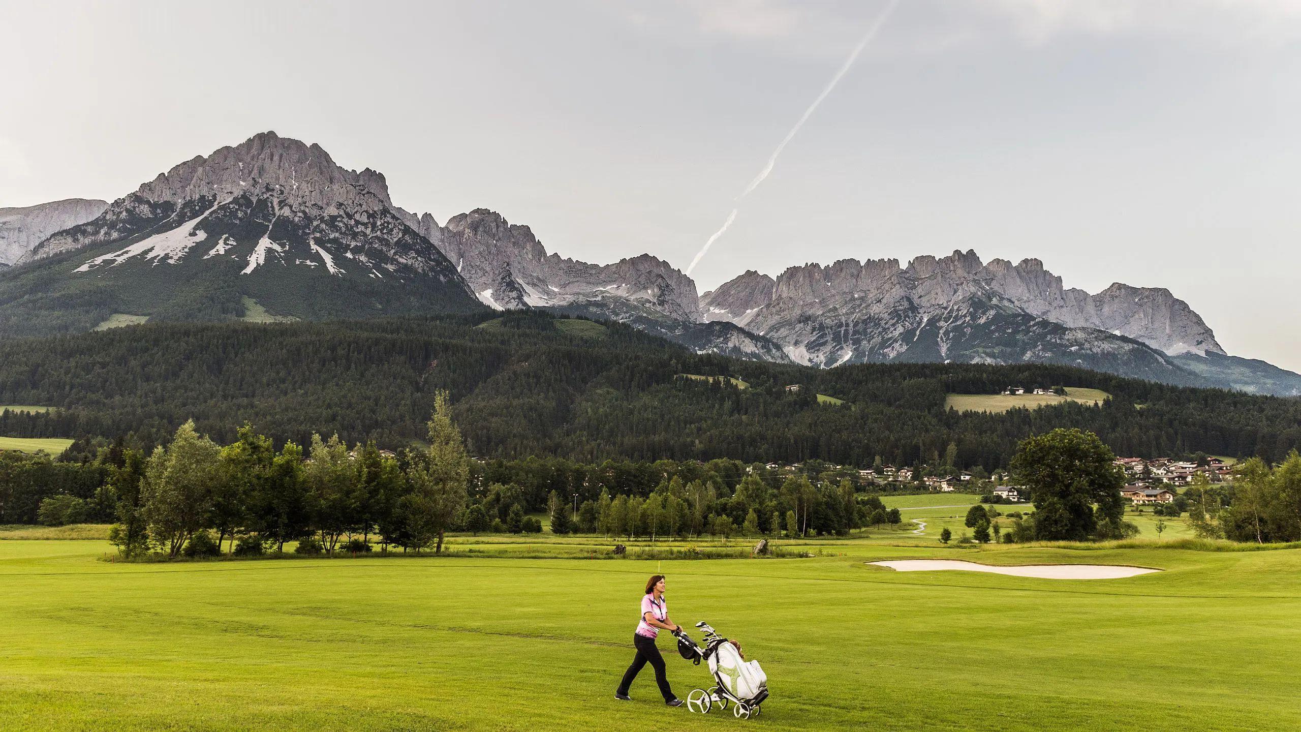 A well maintained fairway nestled with a single sand bunker and mountains towering over in the back