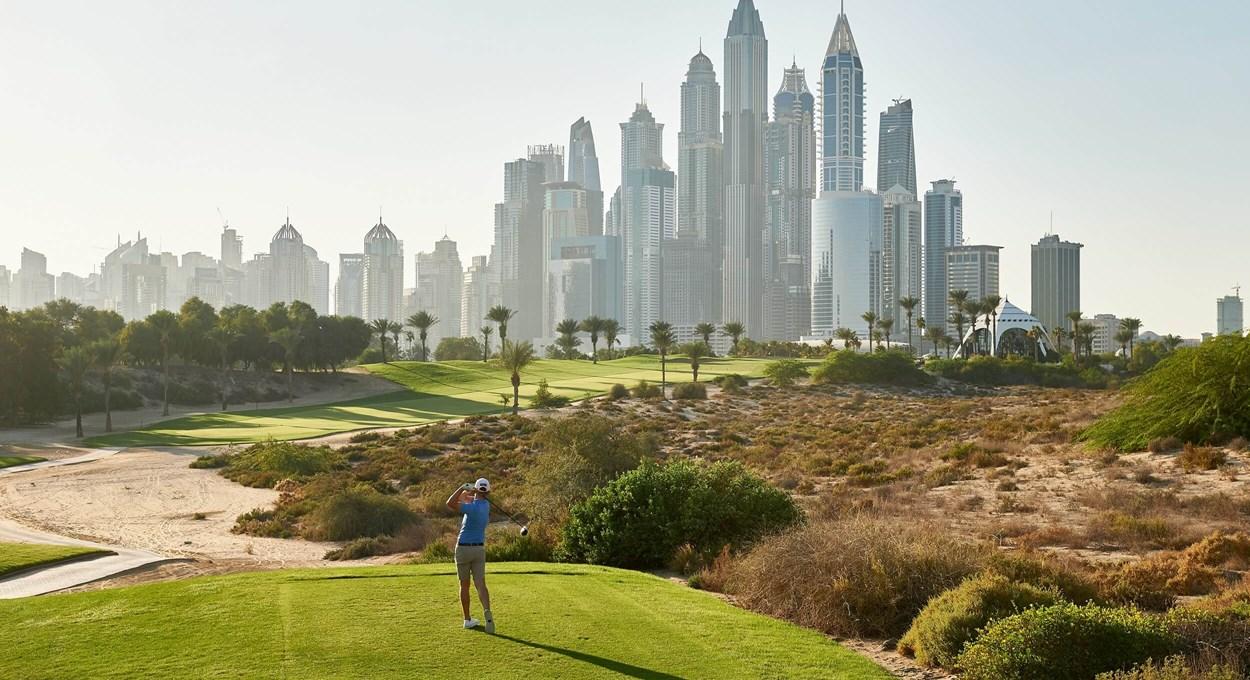A golfer tees off with Dubai's modern skyscrapers looming in the distance.
