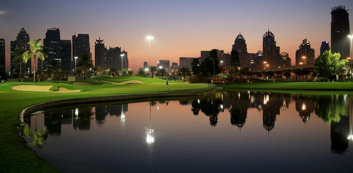 A serene golf course at dusk with city lights reflecting in a pond.