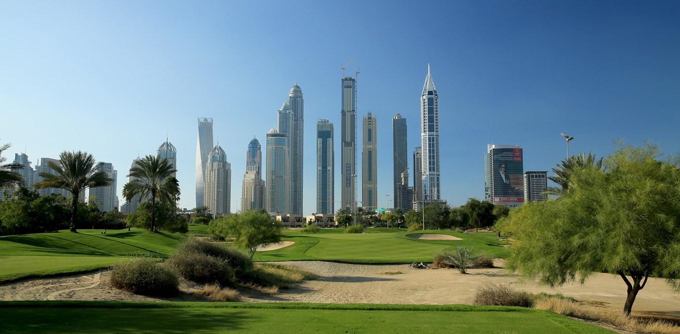 A golf course surrounded by desert landscape with towering Dubai skyscrapers in the background.