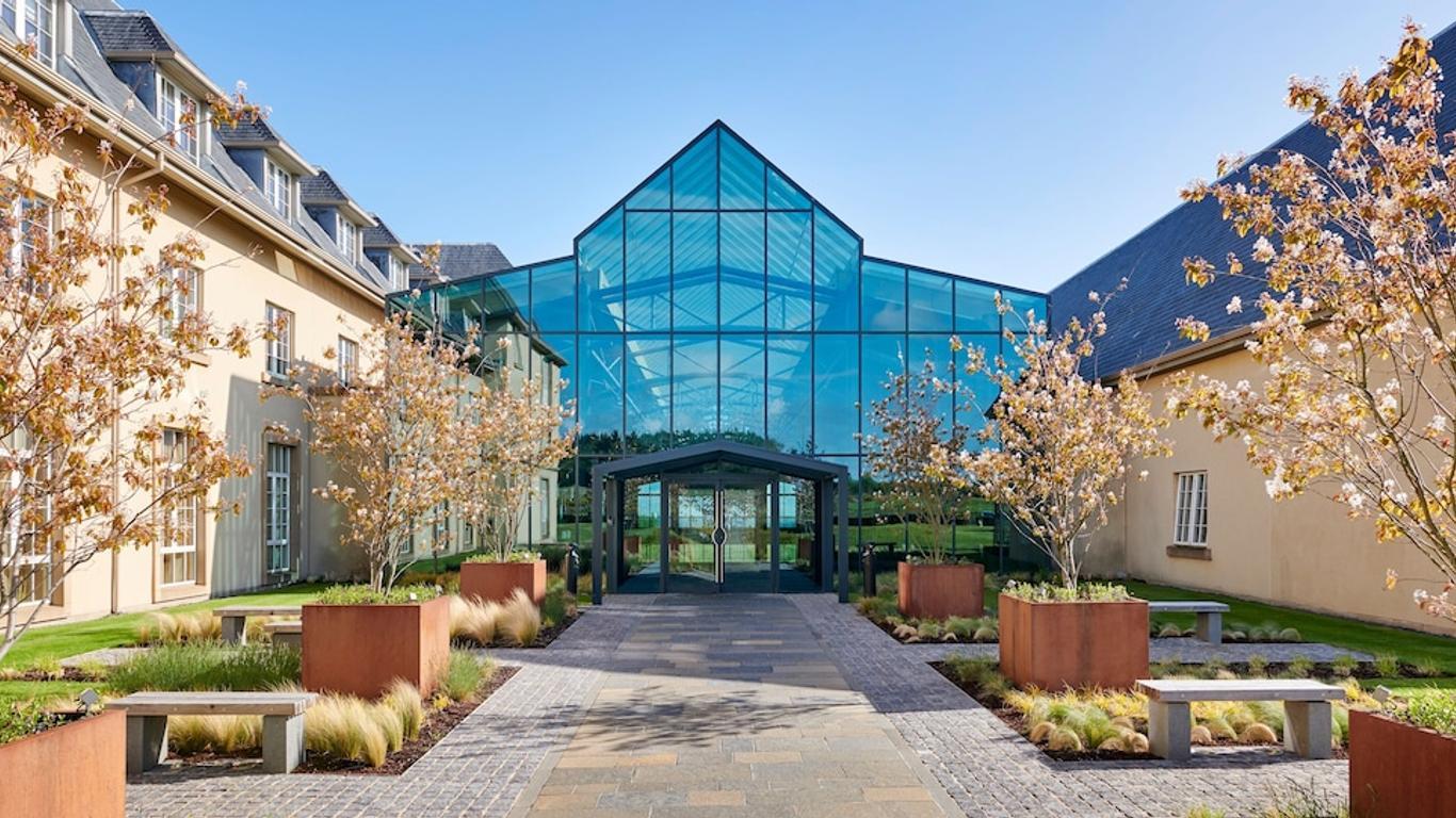 Grand entrance with a glass façade framed by landscaped gardens and pathways.