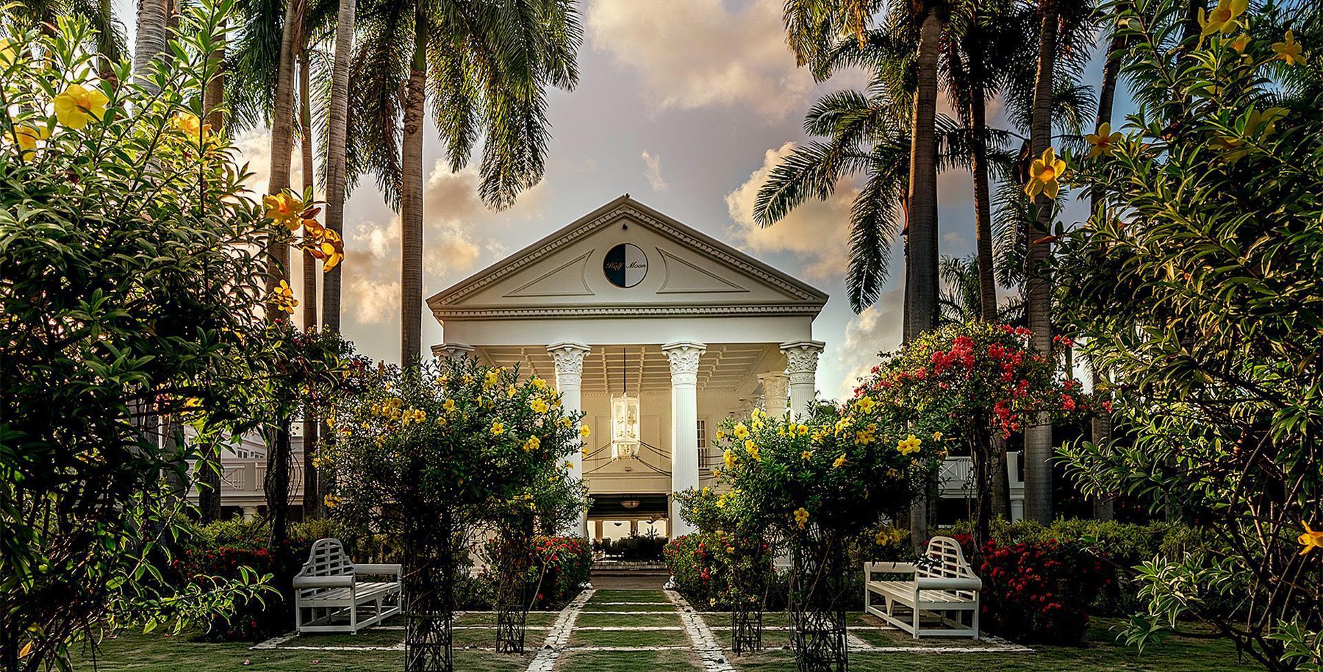 A luxurious garden at the hotel with vibrant flowers surrounding the walk path into an arched building