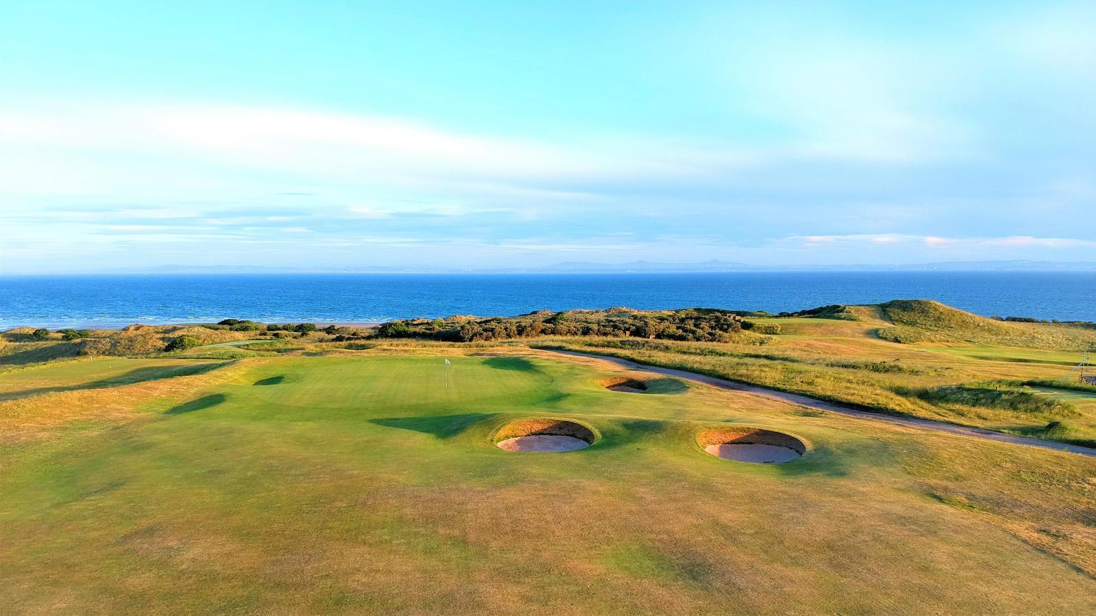 A breathtaking view of the course with rolling fairways leading to the green, set against the stunning coastal backdrop.