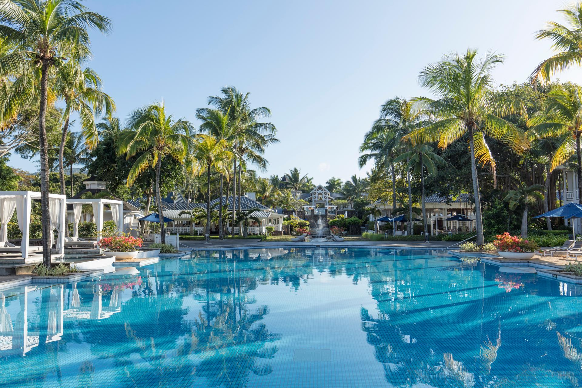 Outdoor swimming pool surrounded by sunbeds, cabanas and palm trees