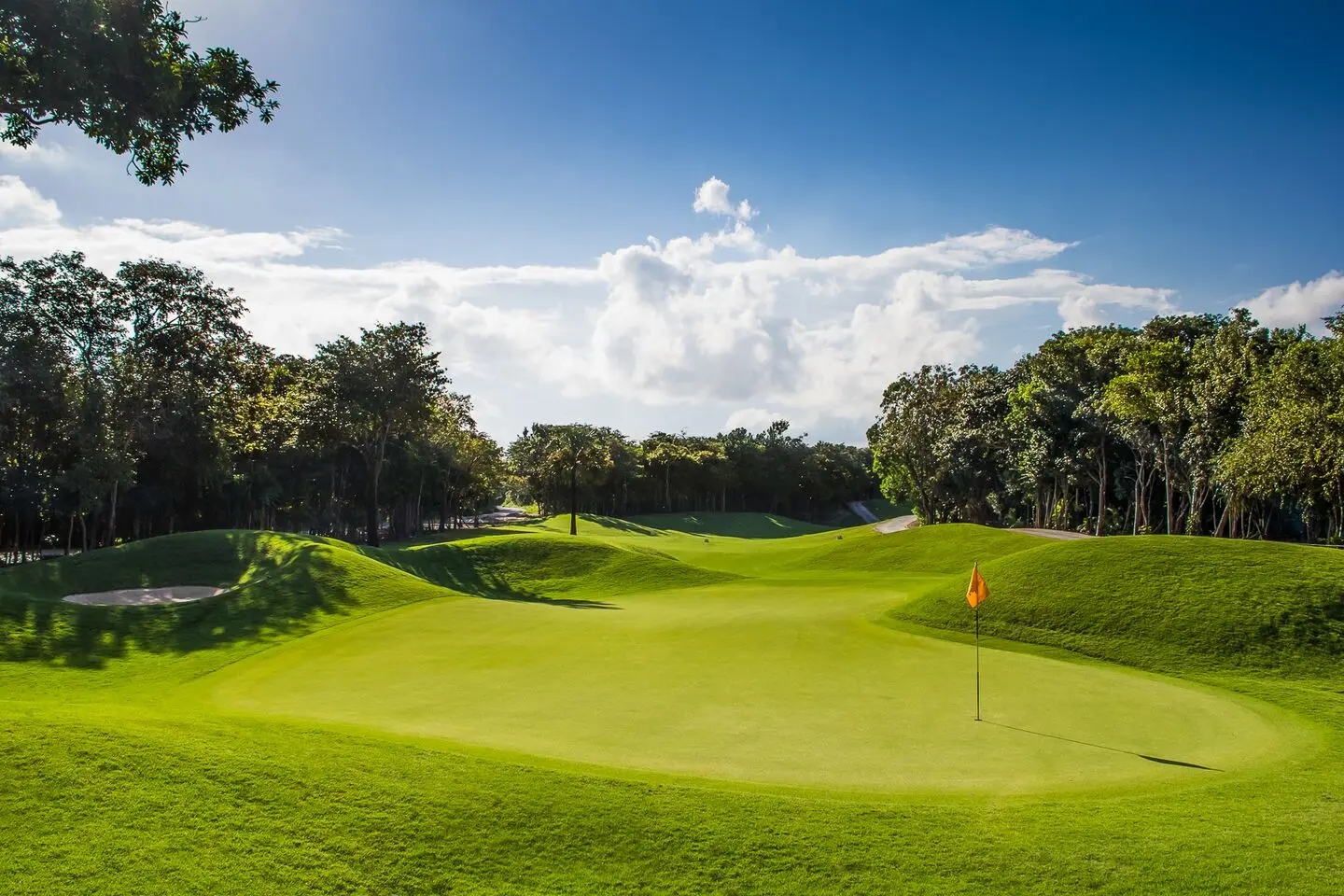 A well-maintained green surrounded by rolling dunes under cloudy blue skies