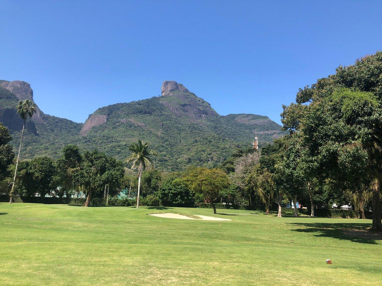 A scenic golf course with palm trees and dramatic mountain peaks under a clear blue sky