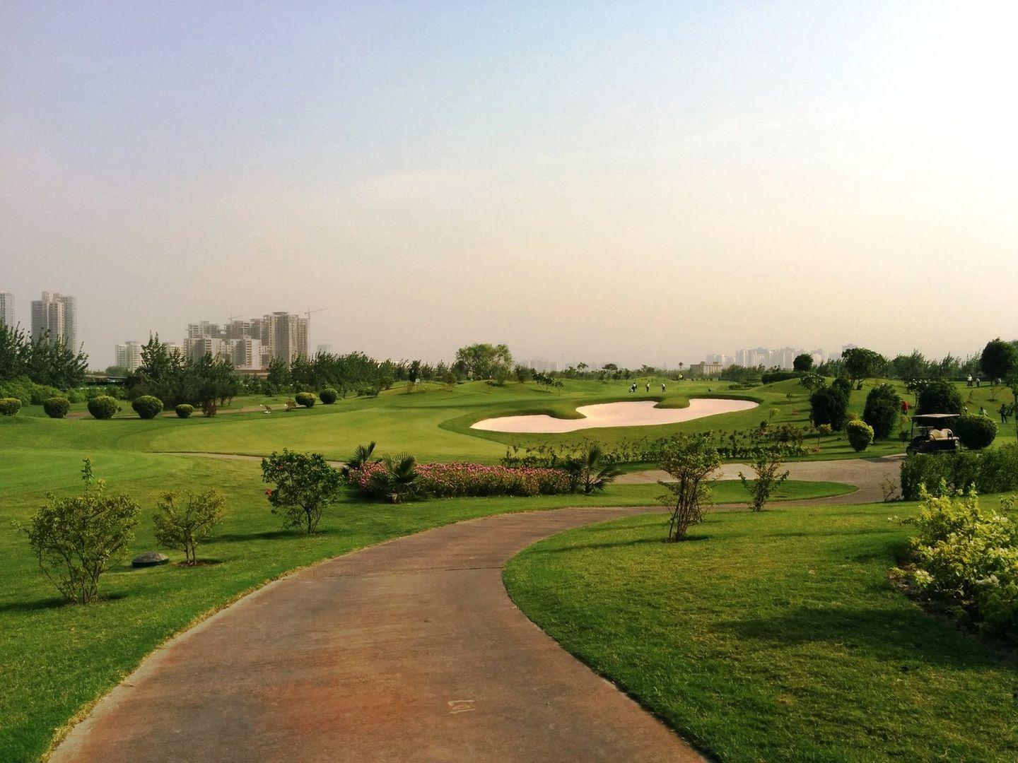 A walkway leading to a large sand bunker next to a smooth green