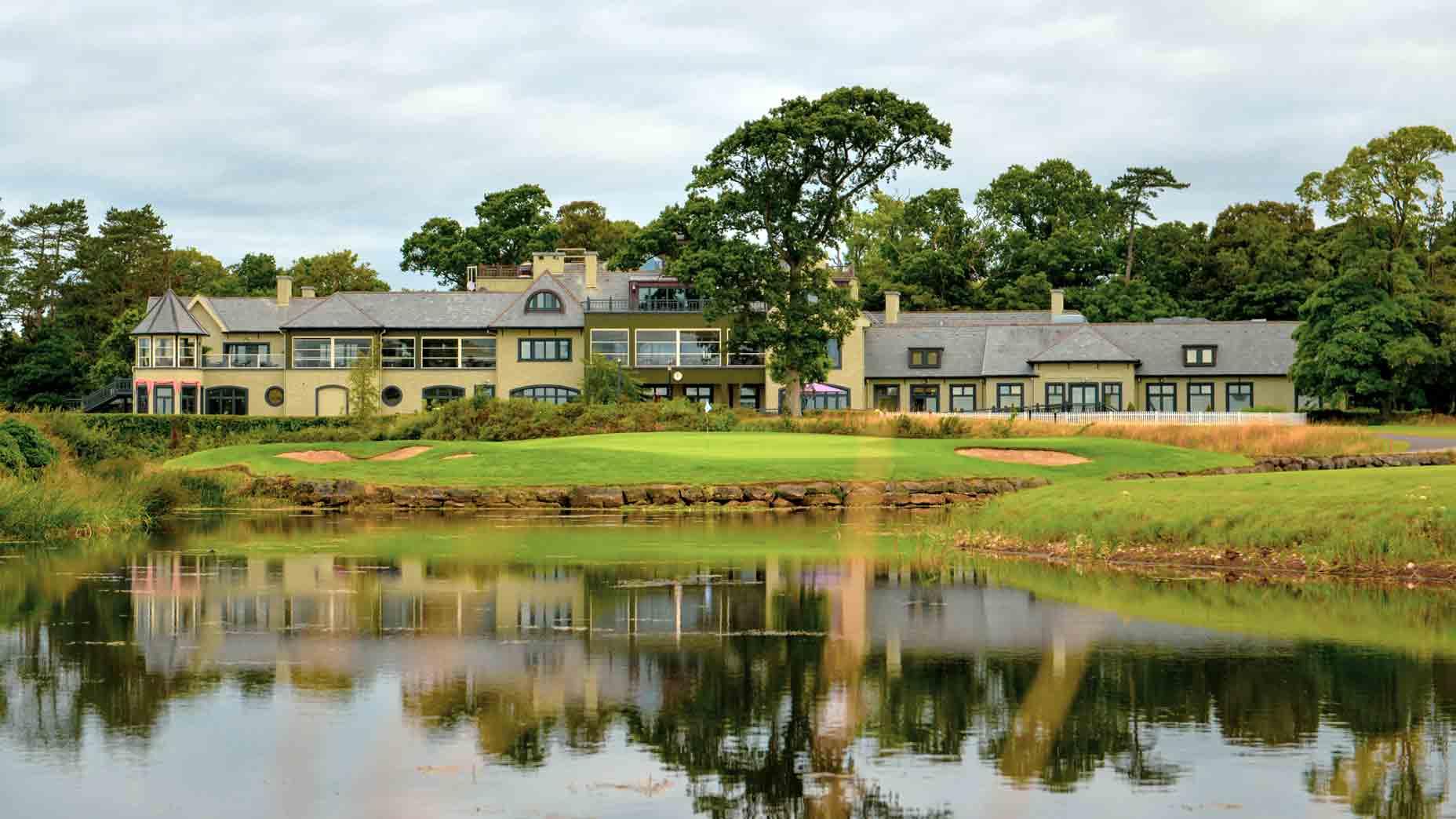 A stunning clubhouse reflected in a calm lake, surrounded by lush greenery and pristine bunkers.