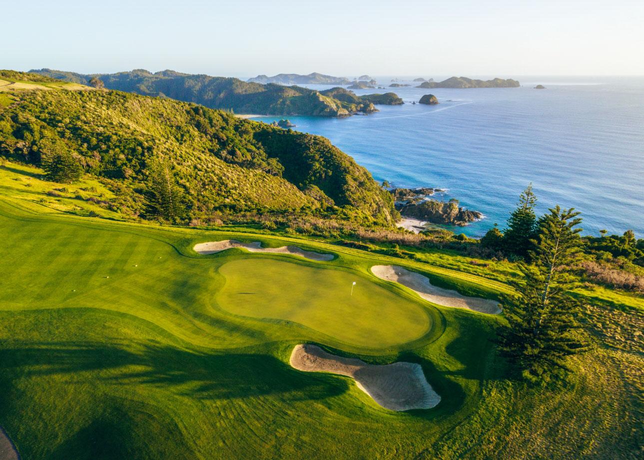 Birdseye view of a smooth green surrounded by sand bunkers with coastal views