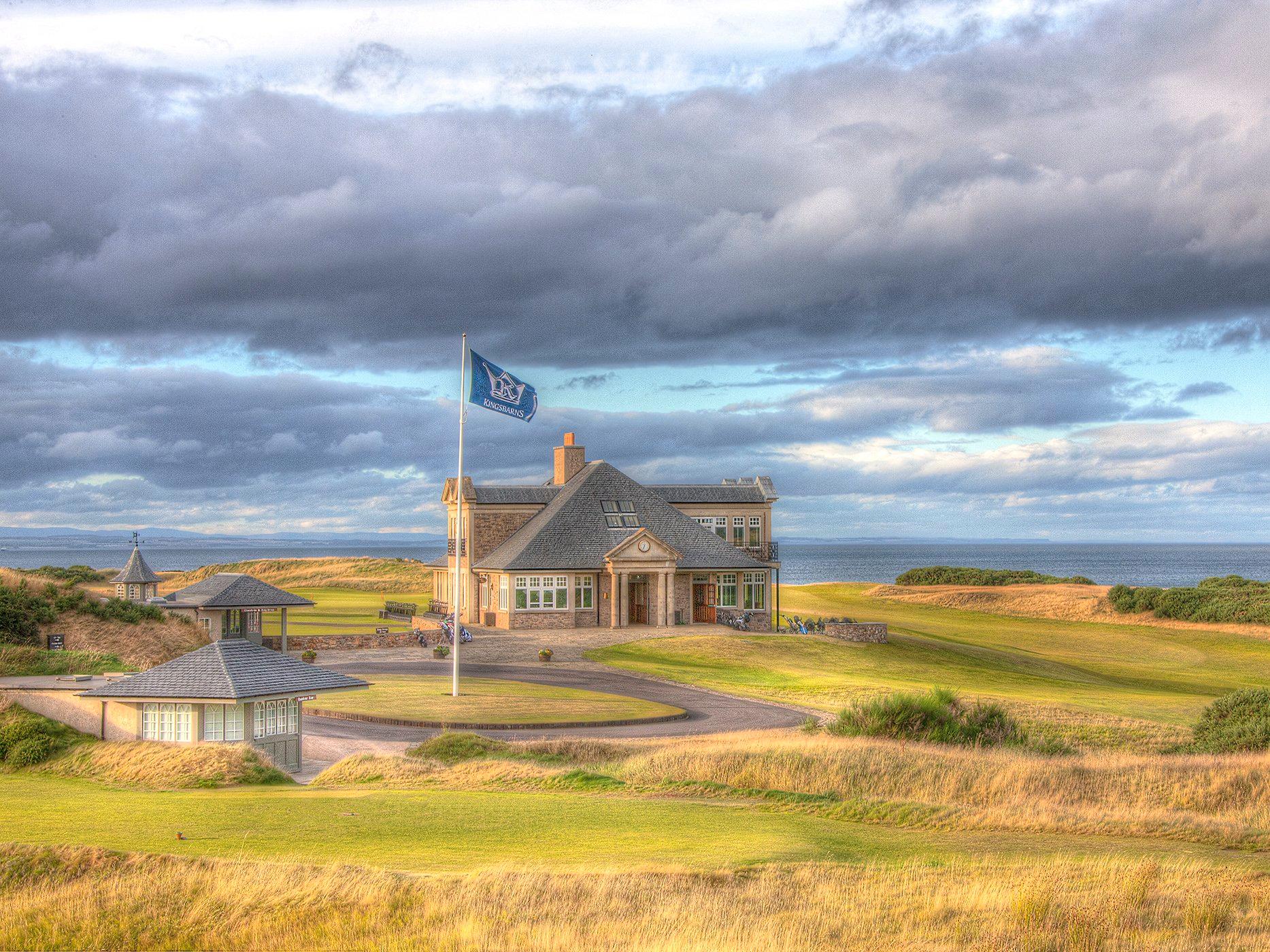 The clubhouse surrounded by golden links, standing tall beneath dramatic skies.