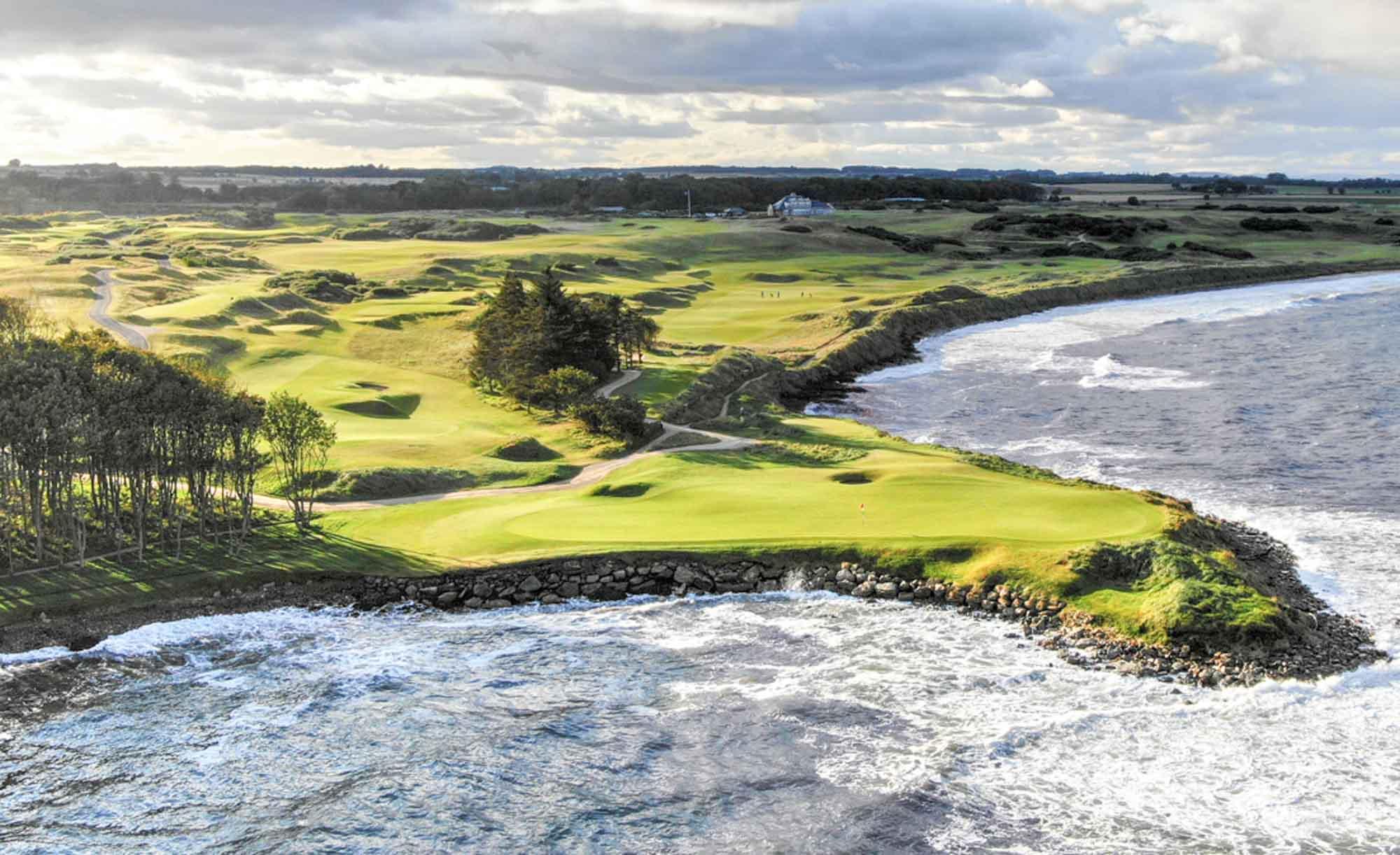 Waves crashing against the shore beside a green perched on a dramatic cliff edge.