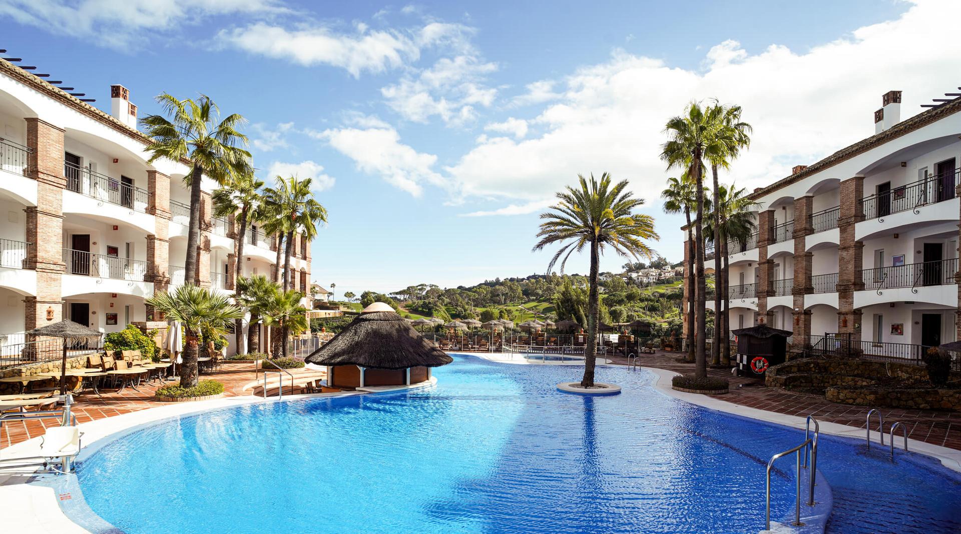 Swimming pool with palm trees around it overlooked by hotel rooms