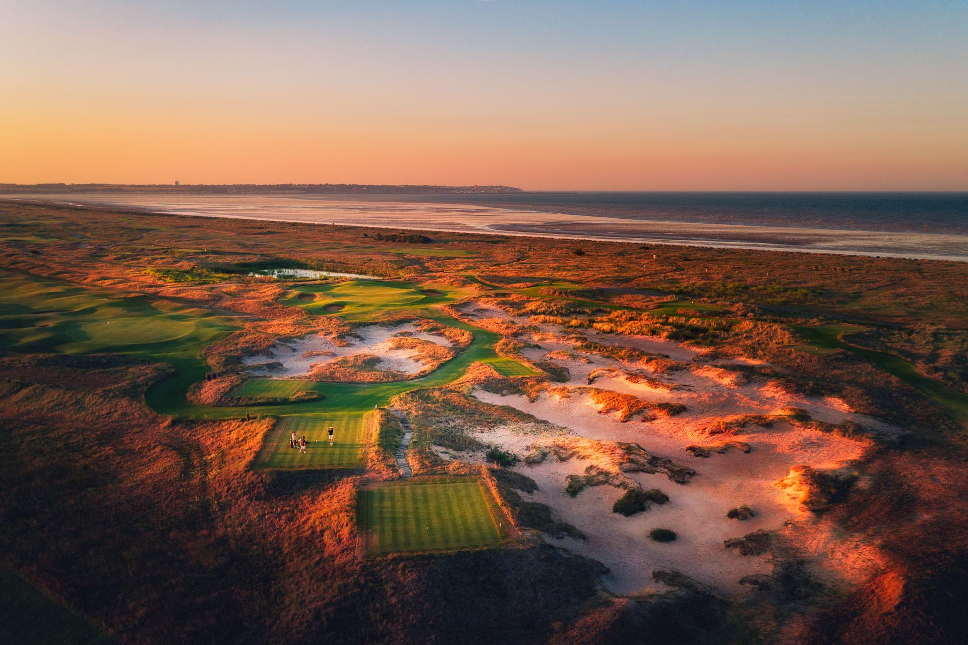 Golfers teeing off under the golden sun surrounded by a rugged rough