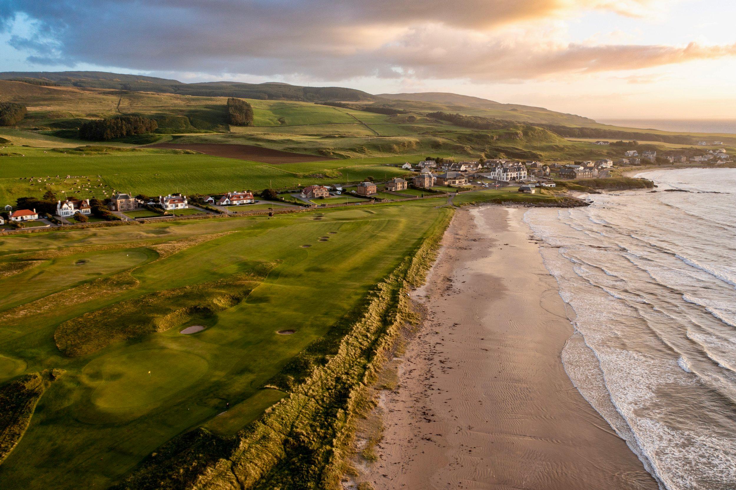 Golf holes sit dramatically atop a cliffside, overlooking the sandy shoreline.