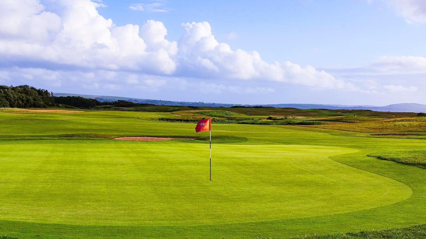 A lush golf course with rolling fairways and a cloudy sky above, set against a scenic landscape.