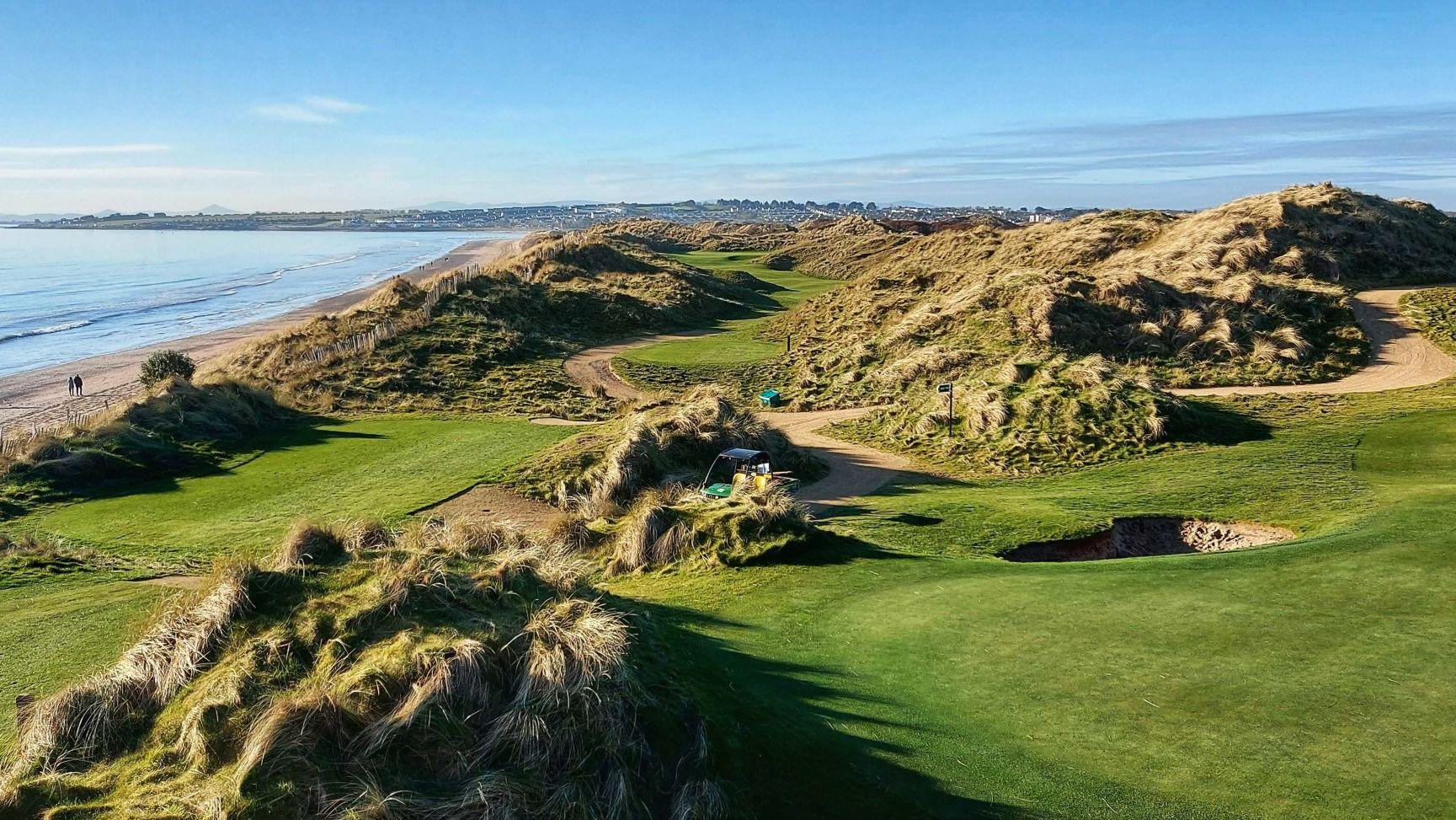 A stunning links golf course runs alongside a sandy beach with rolling dunes and coastal views.