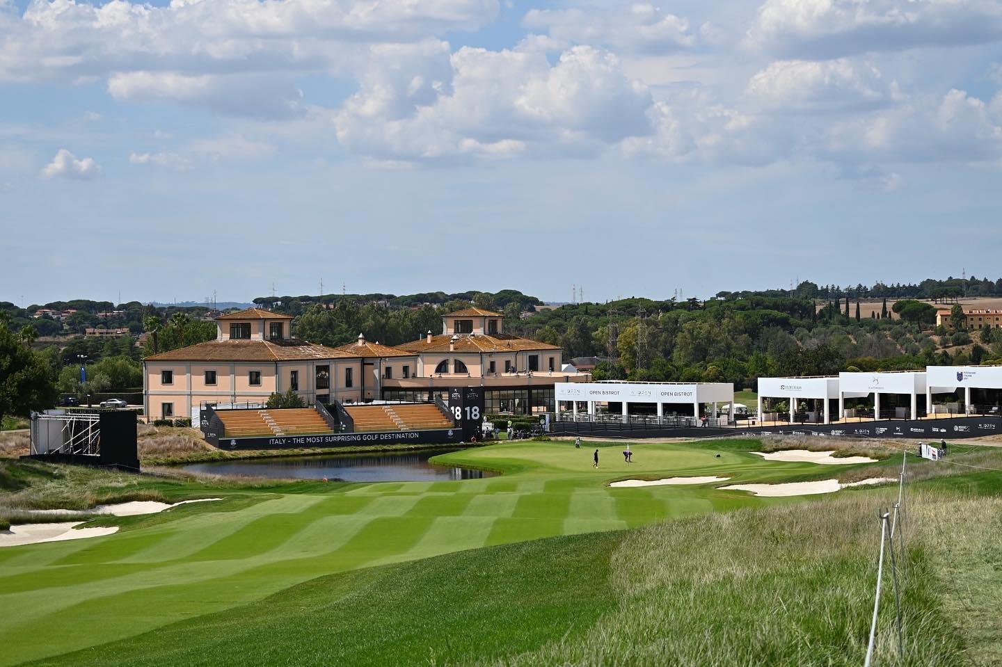 Spectator stands surrounding the green at hole 18 with golfers putting