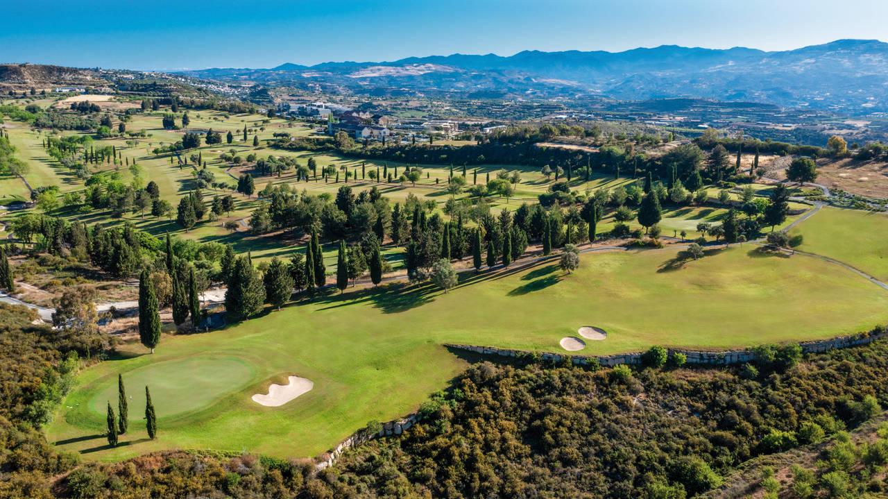 Panoramic aerial view, showcasing the course layout against a mountainous backdrop.