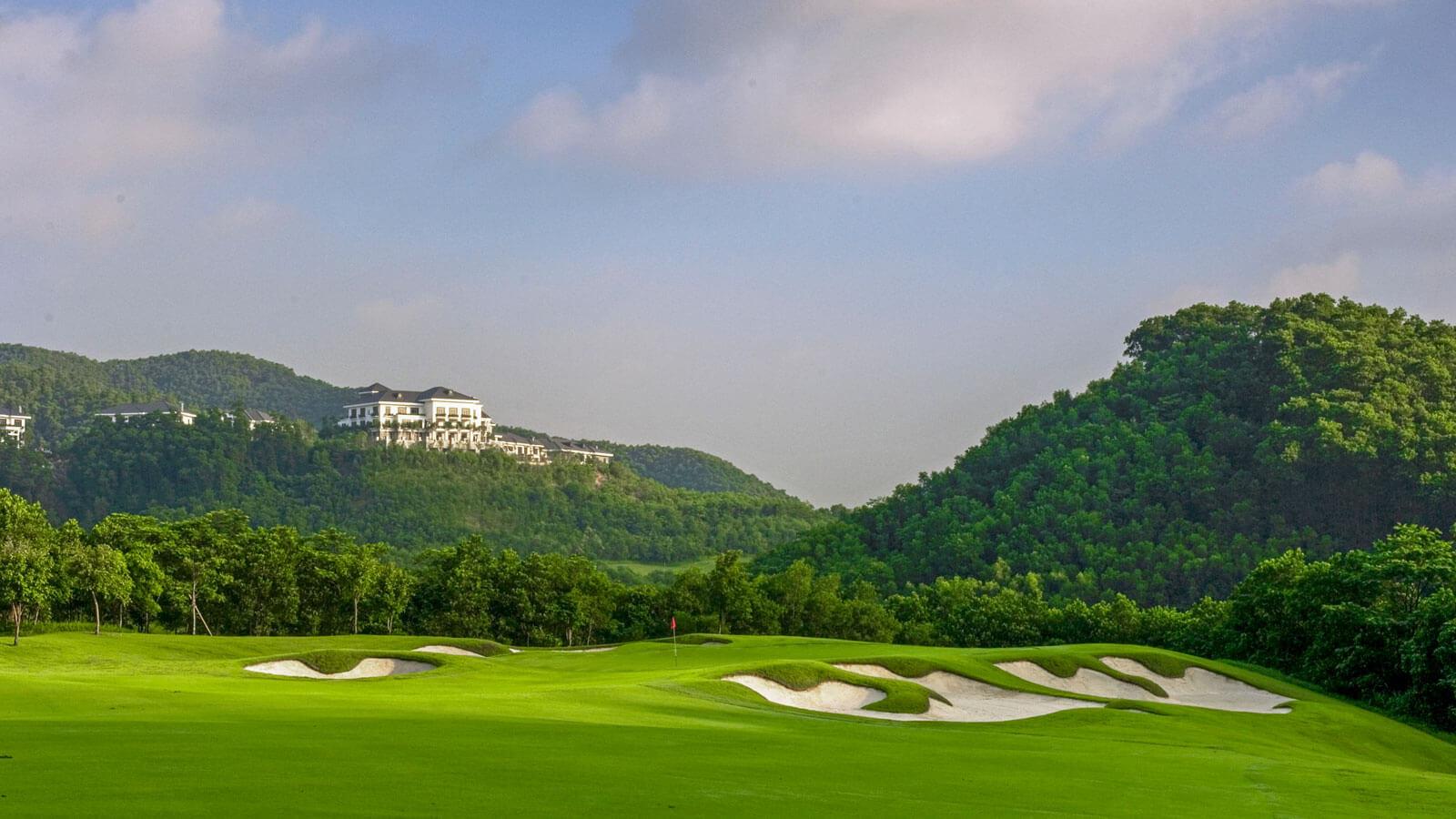 Golf course nestled between green hills with scenic mountain views.