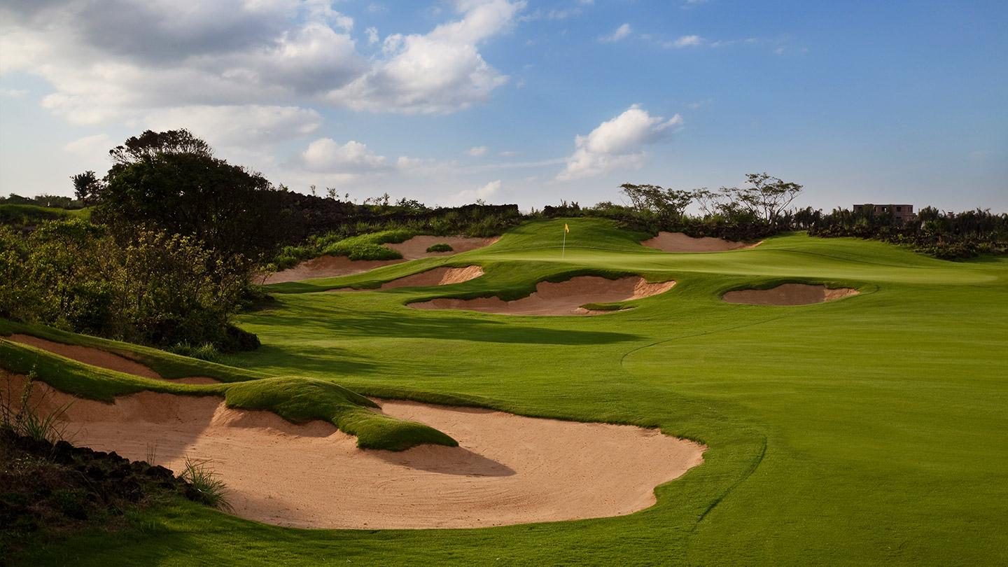 A pristine golf course with golden sand bunkers framed by trees and blue skies.