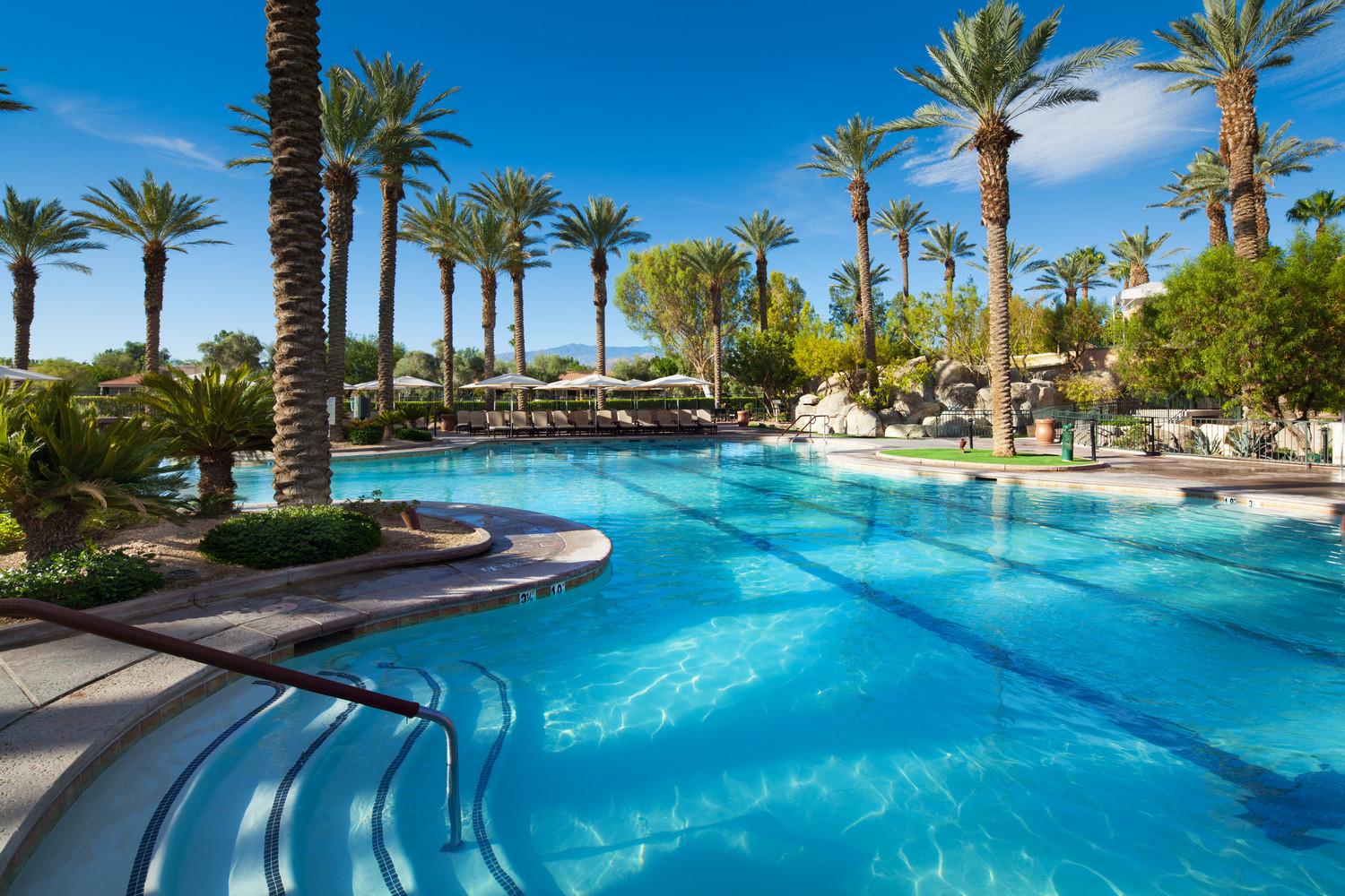 A sky blue swimming pool at the resort reflecting the sun surrounded by palm trees and sunbeds