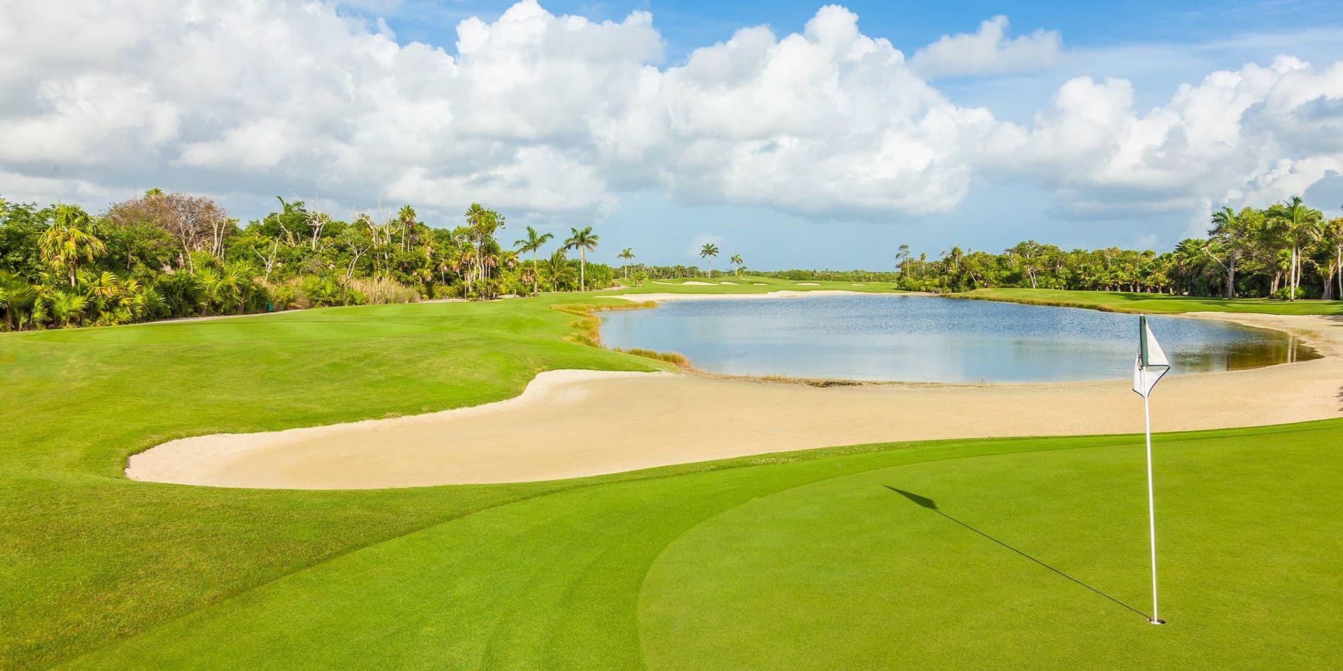 Pristine green with a sand bunker beside a tranquil water feature surrounded by palm trees.
