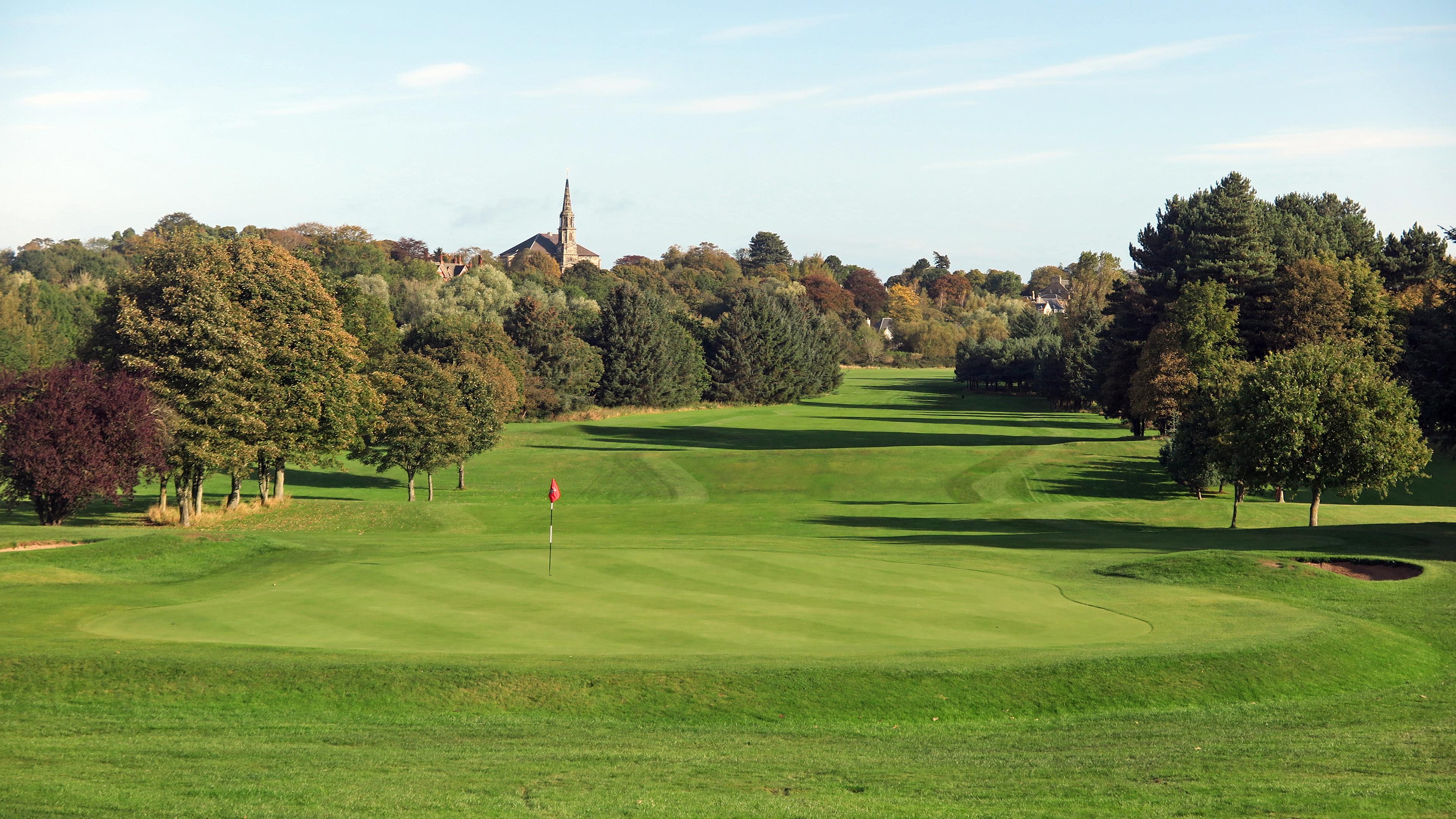 A scenic fairway leading towards a distant church surrounded by trees.