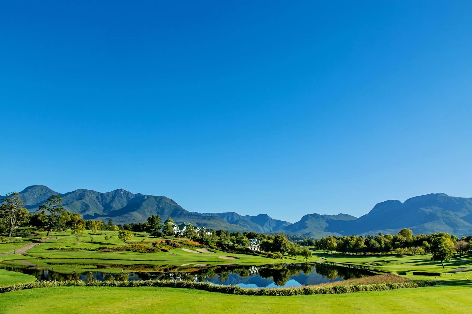 Water hazard reflecting the houses and mountains under blue skies