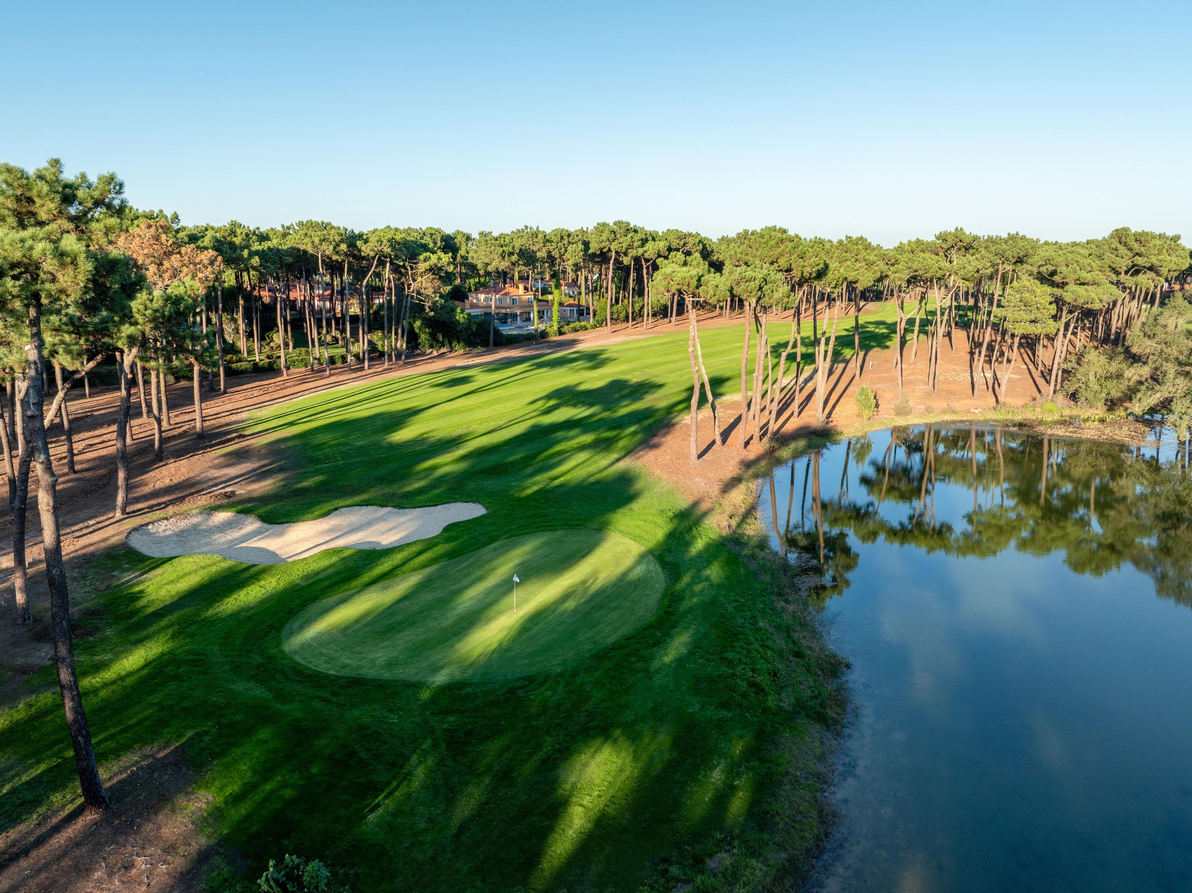 Tree-lined fairway leading to a green with a bunker in front and water behind