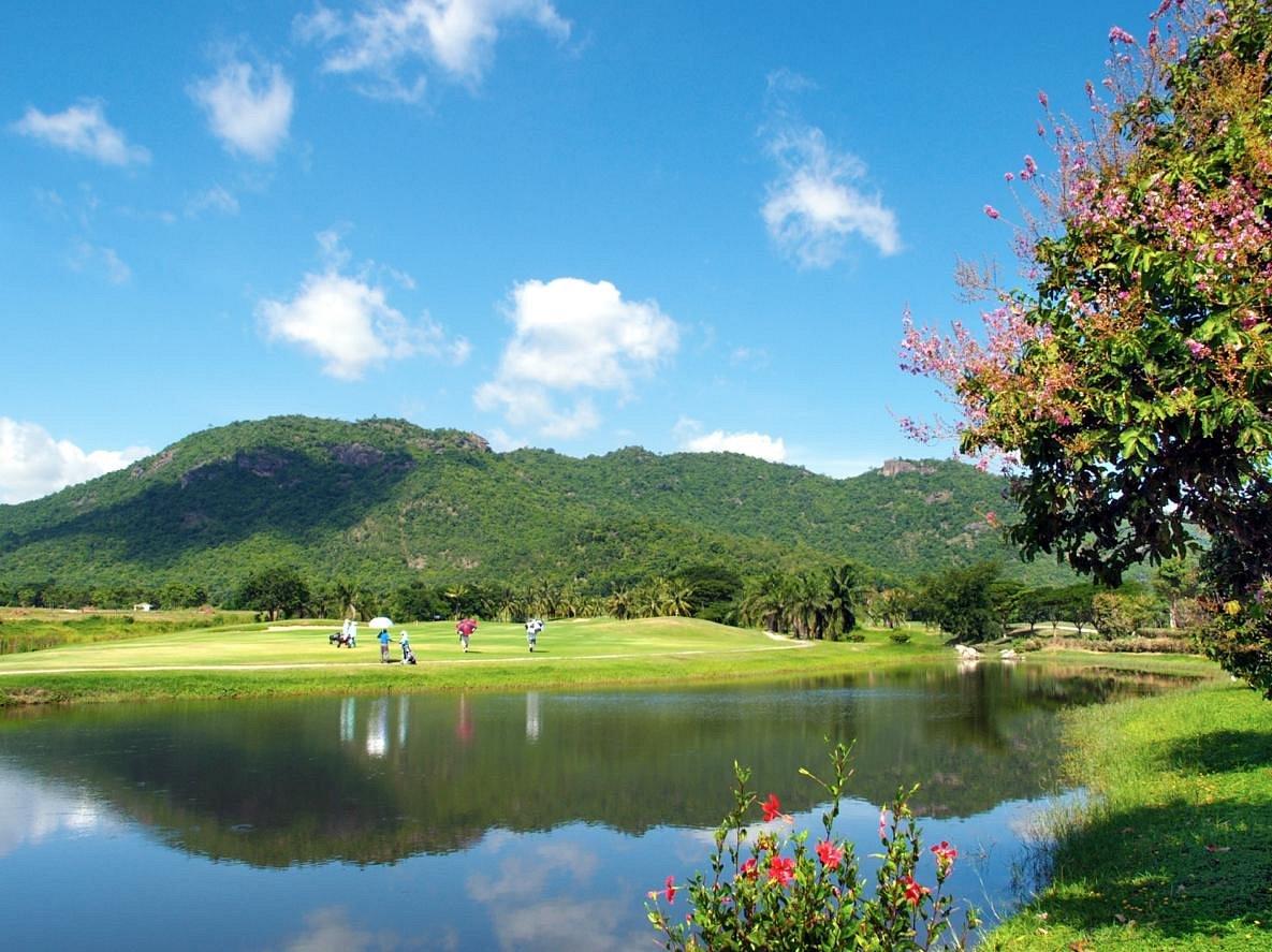 Golfers enjoying their round next to a water hazard reflecting the surrounding mountains